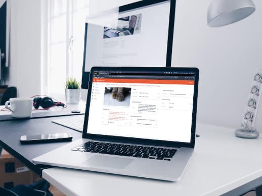 Open macbook on a white desk with a bigger screen in the background, speakers and a light on the right.